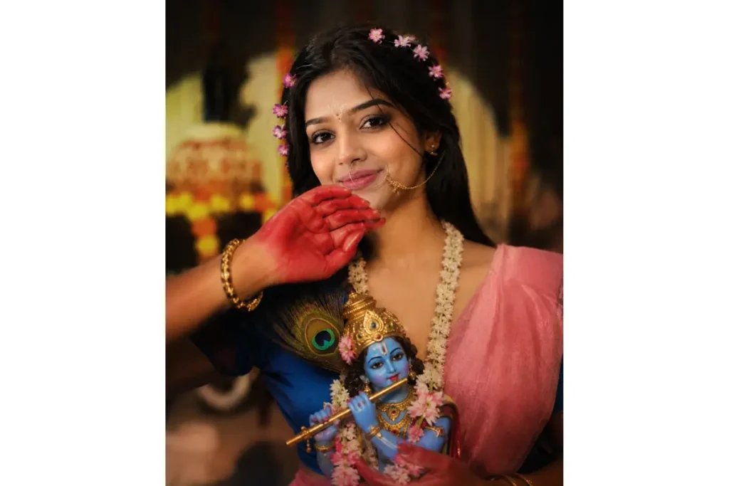 Radharani with red alta on her hands, wearing a pink saree and holding a krishna idol