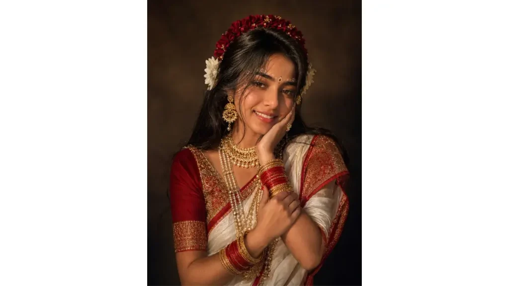Graceful Traditional Radharani Look, its combination of white and red traditional styling, floral crown, gold jewelry, and delicate face art. The gentle hand placement and soft expression create an elegant devotional portrait with a classic Indian aesthetic. radharani look.