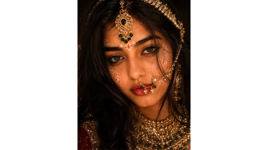 Dreamy Radharani Goddess Aesthetic, the expressive greenish-brown eyes, floral face decorations, ornate gold jewelry, pearls, and green gemstones. The dreamy vintage lighting and dark background give the portrait .