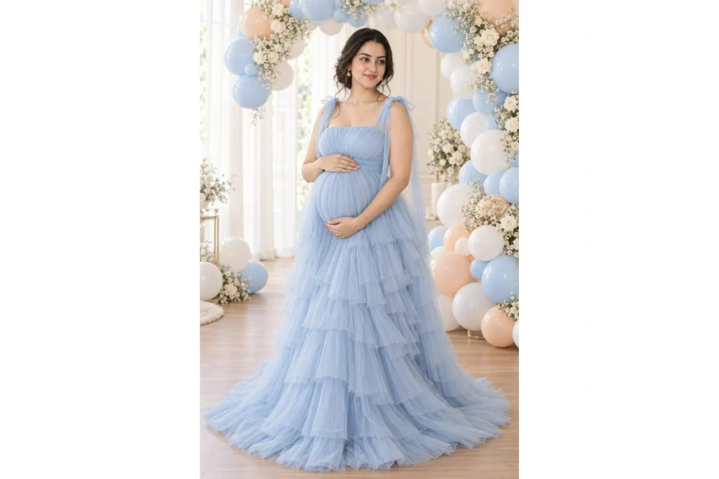 Pregnant woman in a pastel blue flowing gown standing in a dreamy studio decorated with blue and white balloons and flowers