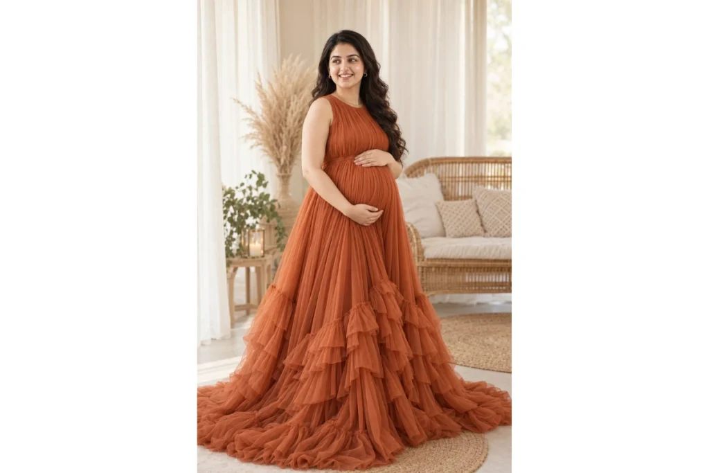 Pregnant woman in a flowing orange maternity gown standing indoors with her hands gently resting on her baby bump
