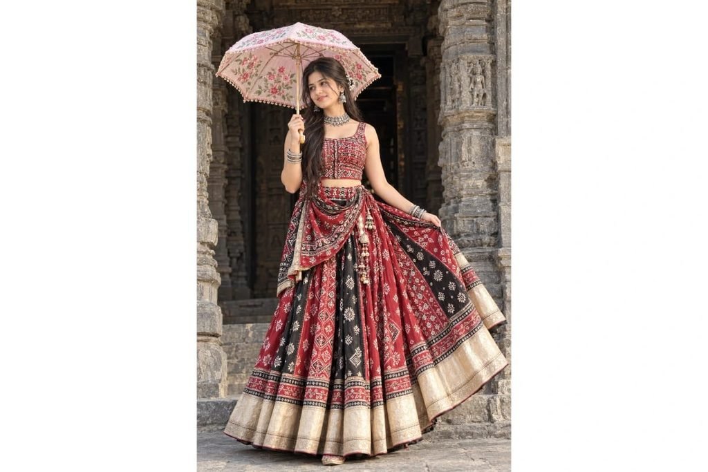 SEO-Friendly Alt Text: Red and black Gujarati Navratri chaniya choli with traditional embroidery, golden lehenga border and floral umbrella, elegant Garba outfit for girls at an ancient stone temple