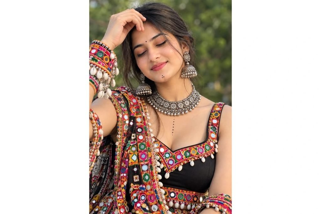 Close-up Gujarati Garba portrait of a girl wearing a black mirror-work chaniya choli, traditional silver choker necklace, jhumka earrings and colorful bangles with eyes gently closed