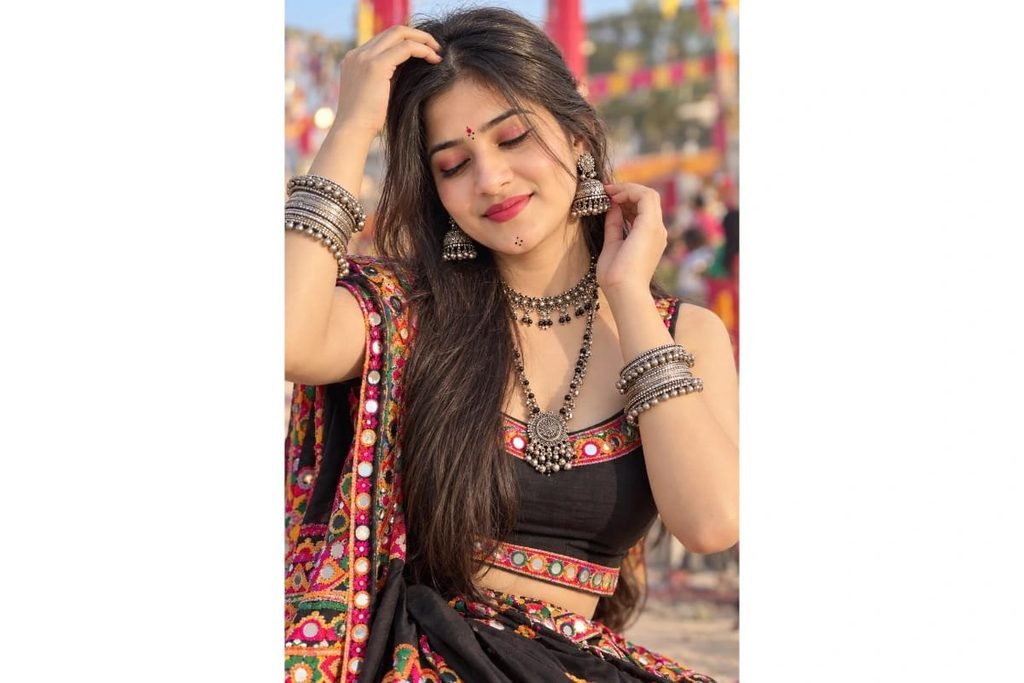 Gujarati Garba girl wearing a black mirror-work chaniya choli with colorful embroidered borders, traditional silver jewelry and bangles, posing with eyes gently closed for Navratri