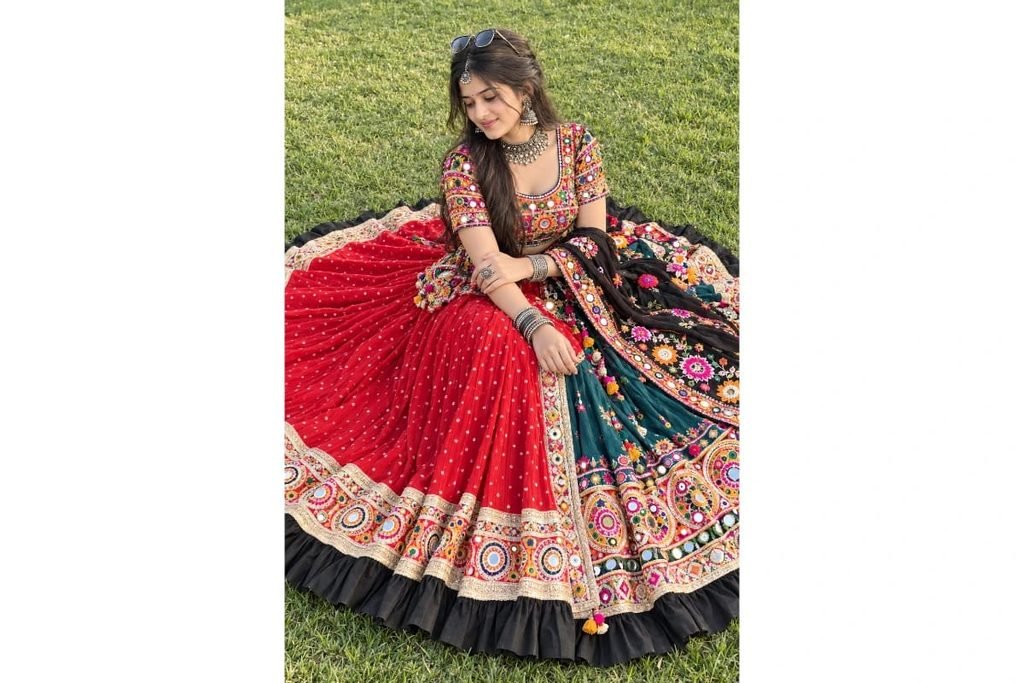 SEO-Friendly Alt Text: Colorful Gujarati Navratri lehenga choli with a red flared skirt, black embroidered dupatta and vibrant traditional mirror-work designs, festive outfit inspiration for girls on green grass