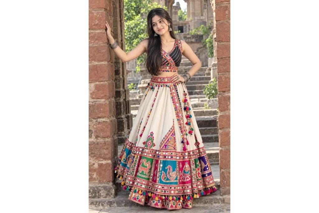 SEO-Friendly Alt Text: Ivory Gujarati Navratri lehenga choli with colorful traditional patchwork embroidery and mirror work, festive Garba outfit for girls at a heritage haveli